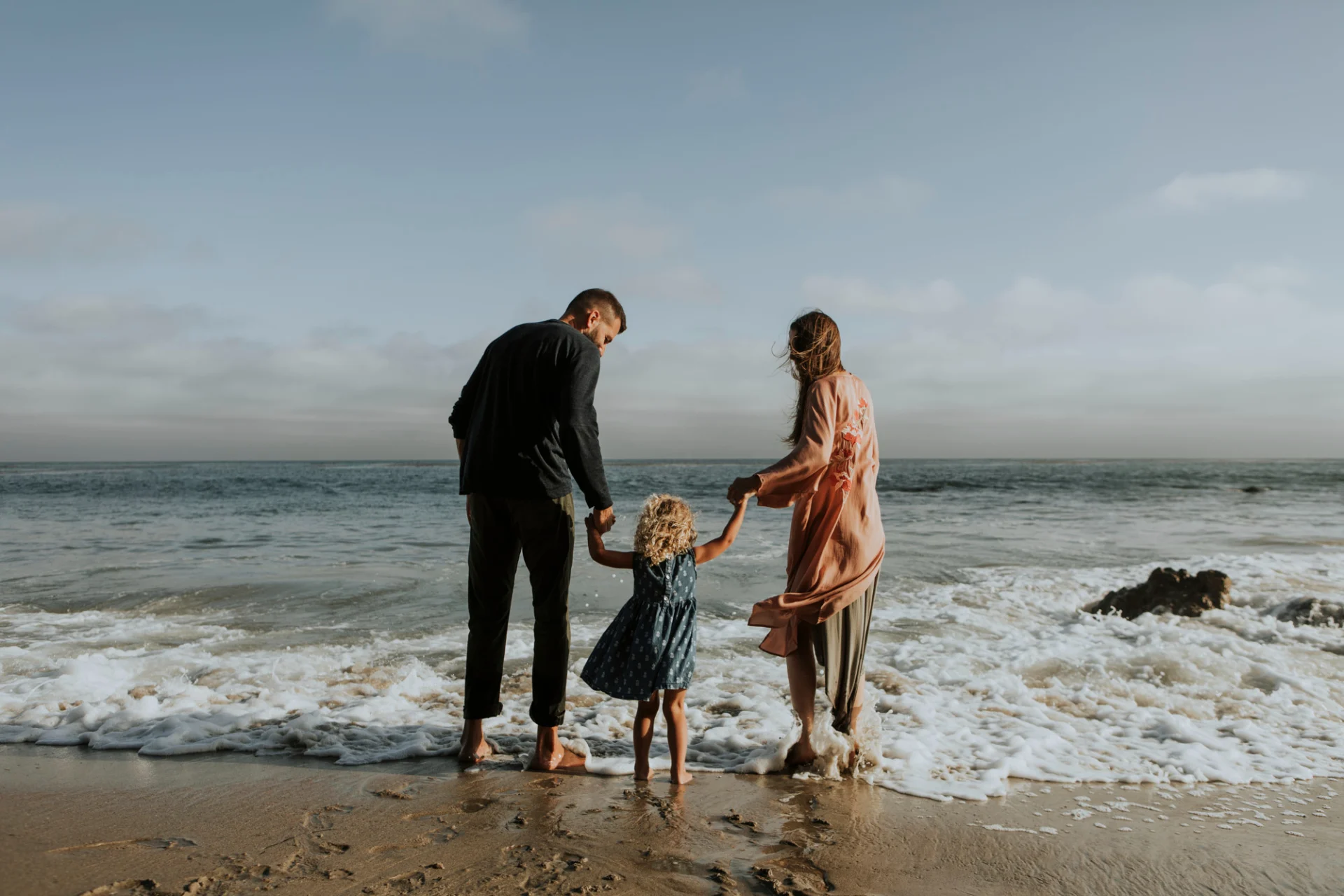 A couple on the beach with their daughter between them and holding their hands.