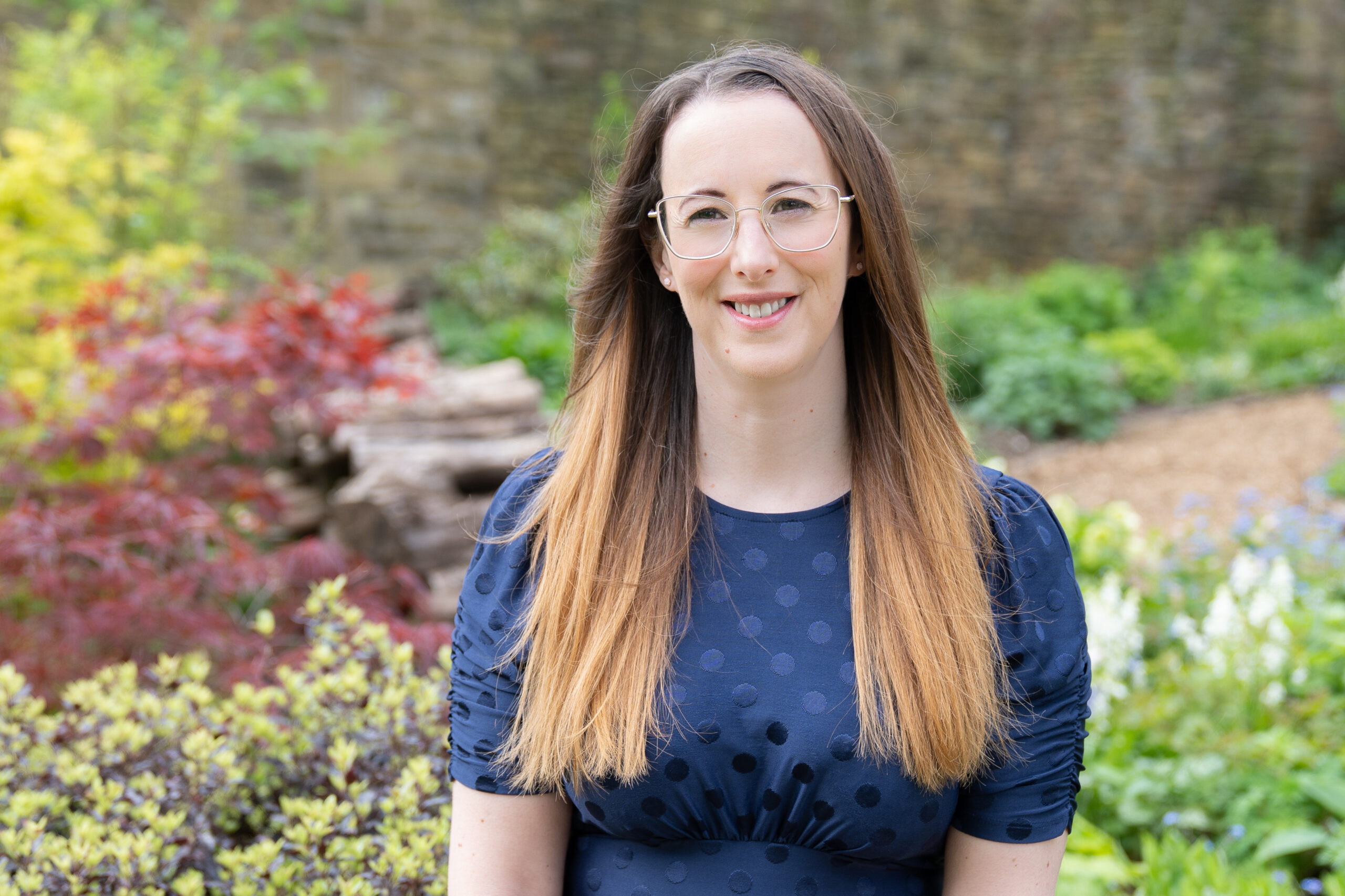 Picture of Fiona Morgan our will writer. Stood in a lovely garden, wearing a blue dress.