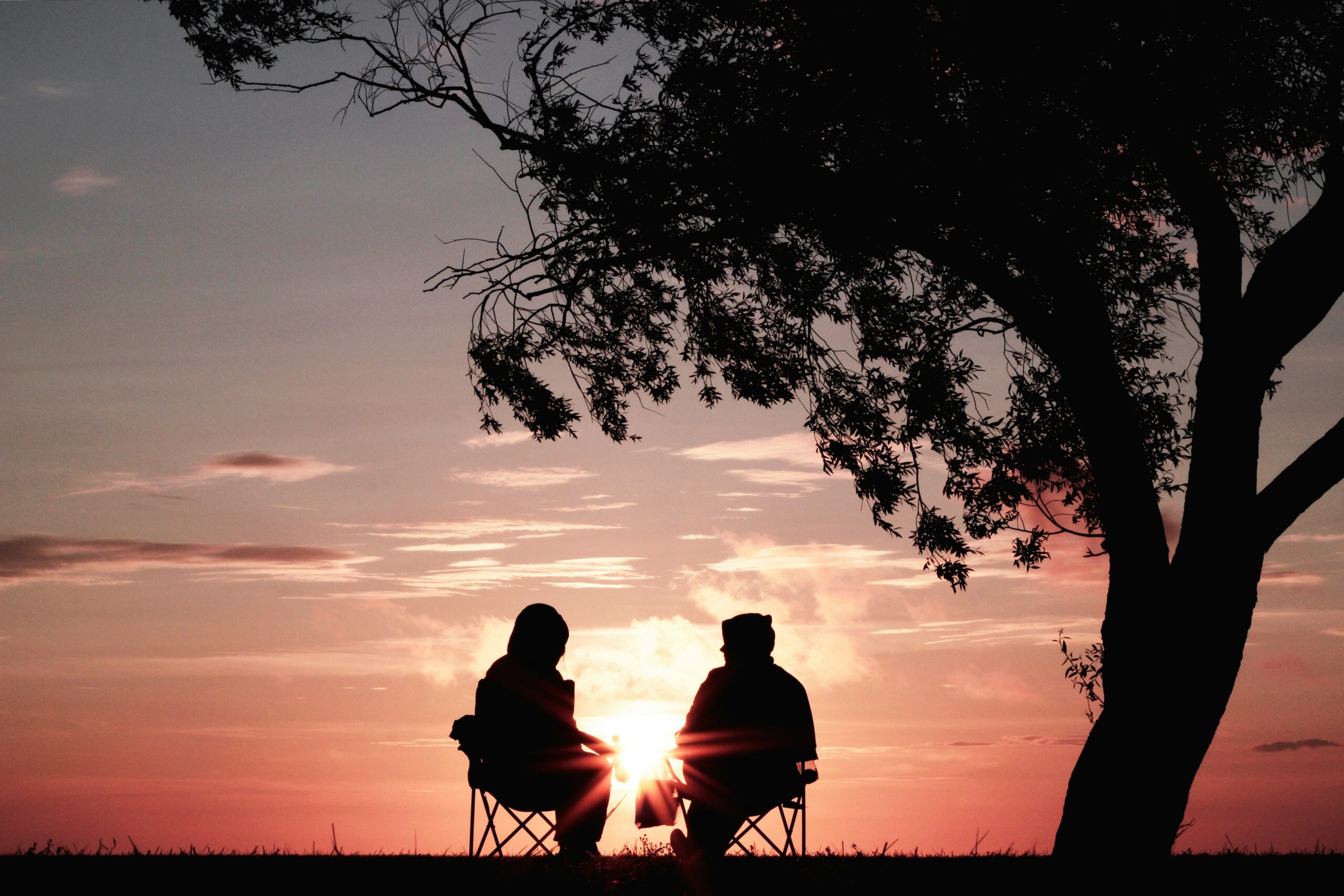 A couple sat on chairs outside with a beautiful sunset behind them. They have peace of mind as their powers of attorney are in place.