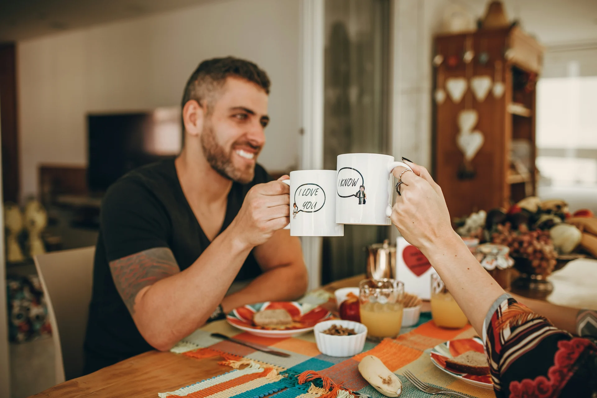 A couple clinking mugs across a table. They've put their wills in place as they are co-habiting and not married.