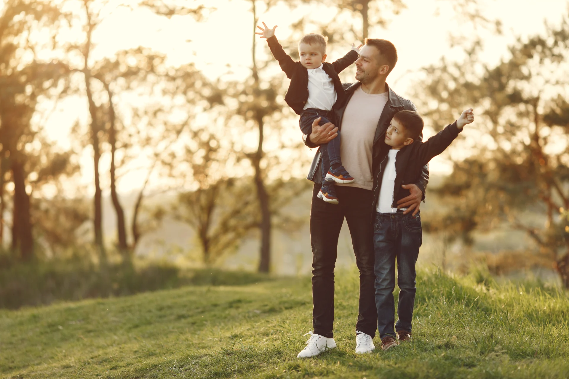 A guy with two sons standing on grass with trees in the background.